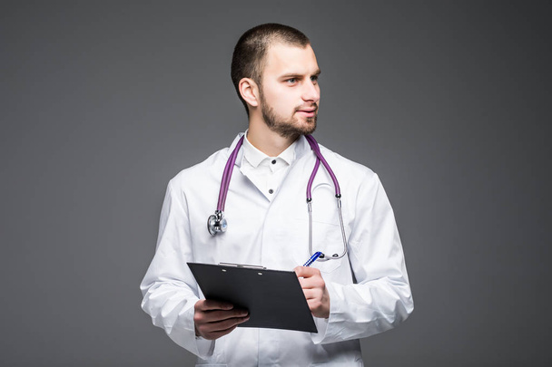 Portrait male doctor wearing a medical suit hang on stethoscope and holding clipboard isolated on gray. Doctor concept. - Fotoğraf, Görsel