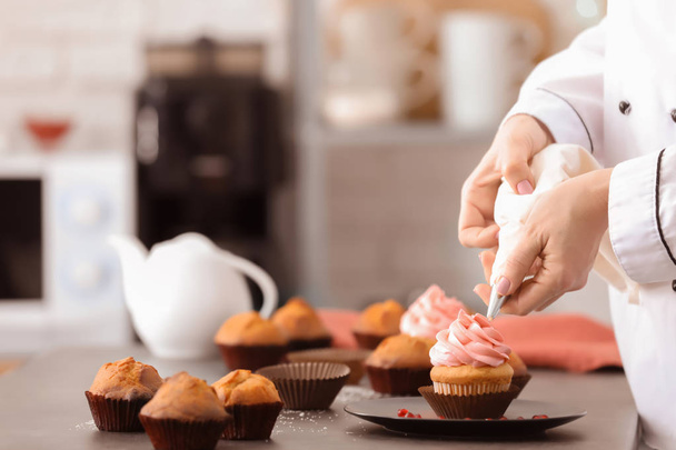Chef decorating tasty cupcake with cream at table - Foto, afbeelding