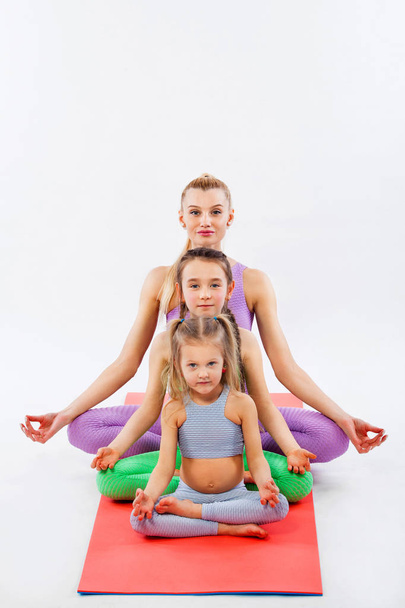 Hatha yoga. Kids fitness . Young mother Instructor and daughters exercise gymnastic together. Isolated on white background. Family look. - Photo, Image