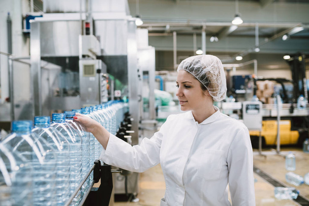 Young woman worker checking robotic line for bottling and packaging pure drinking water into bottles and canisters - Foto, Bild