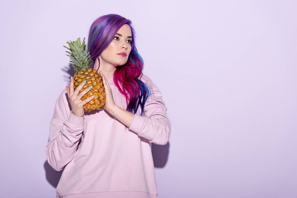 beautiful young woman with colorful hair and pink sweatshirt holding pineapple - Foto, Imagen