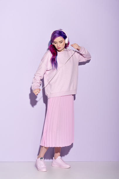 Dancing young woman with purple hair in pink clothes listening music with wired headphones - Fotoğraf, Görsel