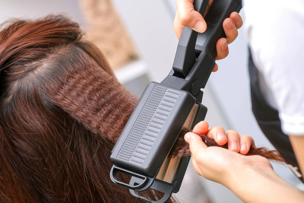 Gros plan des mains stylistes avec fer à lisser coiffant femme
  - Photo, image