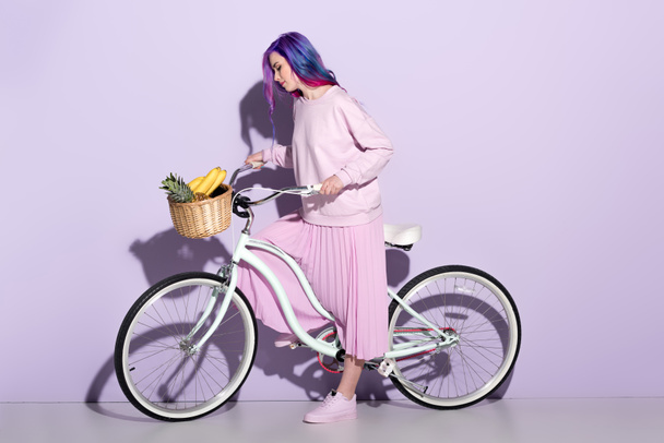 attrayant jeune femme en vêtements roses sur vélo avec ananas et bananes dans le panier
 - Photo, image