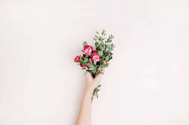 Vrouw hand houd roze bloemen en eucalyptus boeket op witte achtergrond. Achtergrond van de kop van de held van de blog van het voorjaar van plat lag, bovenaan weergave. - Foto, afbeelding