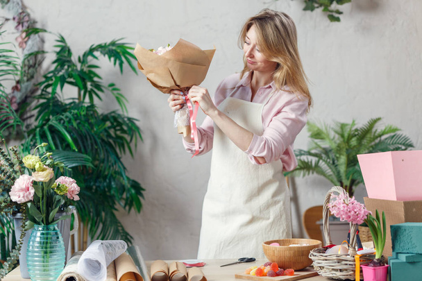 Photo of florist in apron making bouquet at table with marmalade, paper - Фото, зображення