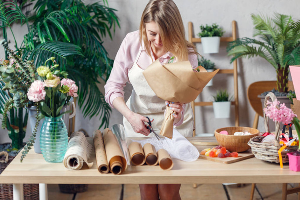 Image of florist woman in apron with bouquet of kraft paper at table with paper - Φωτογραφία, εικόνα