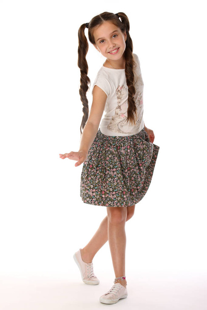 A little girl 12 years old posing in summer clothes. Charming pretty slender young teenager is in a skirt with bare legs. Beautiful brunette child is standing at full length and smiles slightly. - Foto, afbeelding