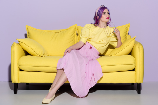 thoughtful young woman sitting on yellow couch - 写真・画像