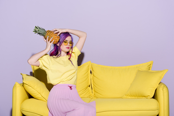 bella giovane donna seduta sul divano giallo e tenendo l'ananas vicino alla testa
 - Foto, immagini
