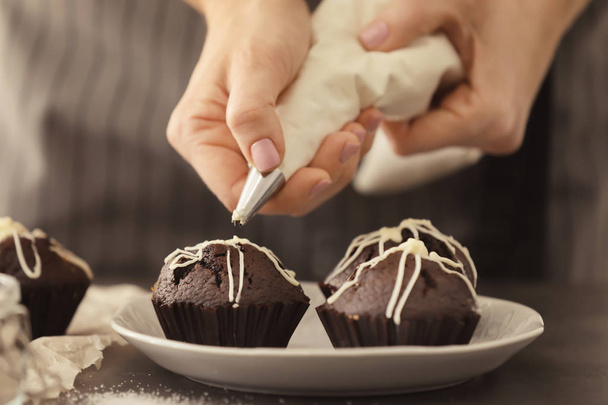 Woman decorating tasty cupcake with frosting at table - Foto, imagen
