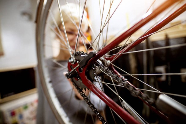kadın kırmızı bisiklet tekerleği atölyede inceleyerek  - Fotoğraf, Görsel