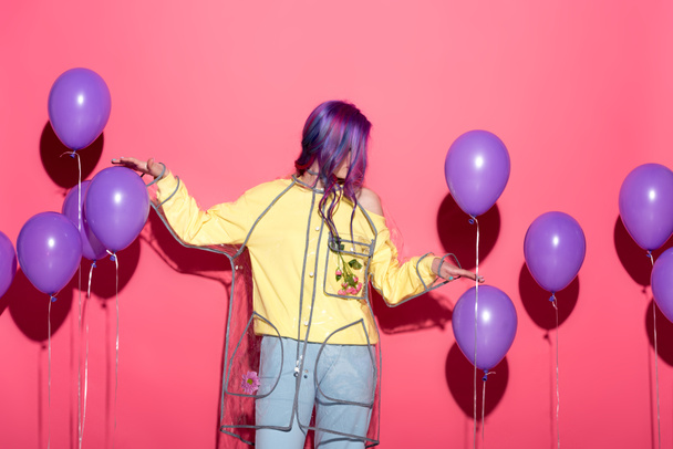 stylish young woman in transparent raincoat with balloons on red - 写真・画像