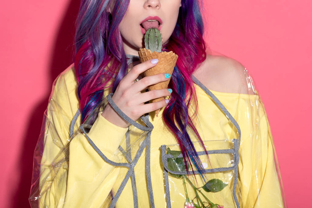 cropped shot of young woman in transparent coat licking cactus in waffle cone - Foto, Bild