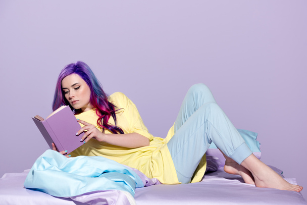 jonge vrouw met kleurrijke haar boek in bed lezen geconcentreerd - Foto, afbeelding