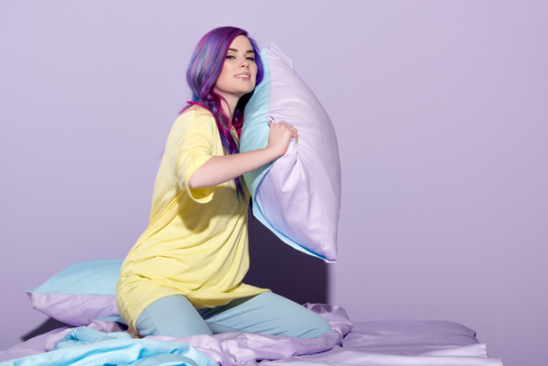 heureuse jeune femme avec des cheveux colorés tenant oreiller au lit
 - Photo, image