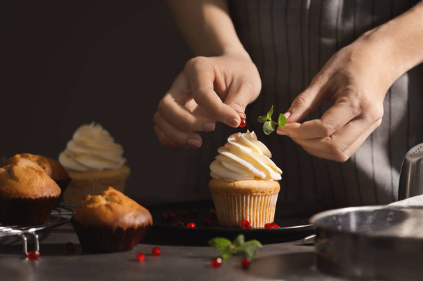 Woman decorating tasty cupcake with mint and pomegranate seeds at table - Φωτογραφία, εικόνα