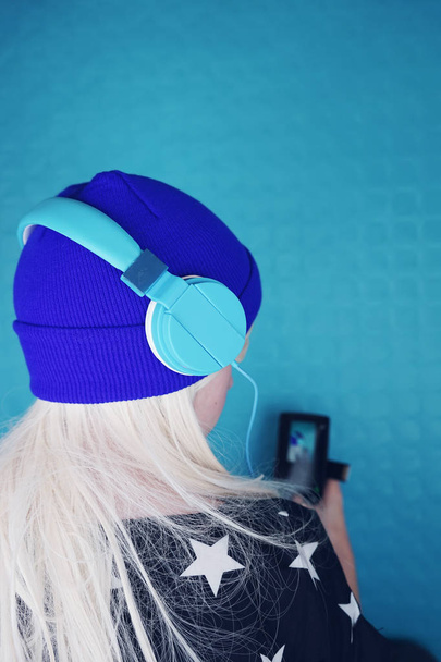 Porträt der jungen blonden Frau in blau Kopfhörer anhören von Musik im Hintergrund - Foto, Bild