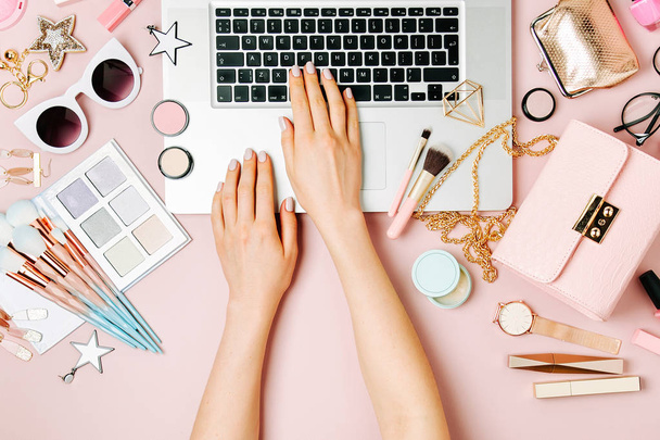 Fashion blogger working with laptop. Workspace with  female accessory, cosmetics products on pale pink table. flat lay, top view - Fotoğraf, Görsel