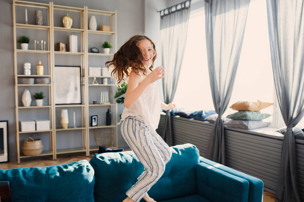 glückliches Mädchen, das am Wochenende morgens zu Hause spielt und im modernen skandinavischen Interieur auf der Couch springt - Foto, Bild