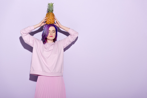 attractive young woman in pink sweatshirt holding pineapple on head - Фото, изображение
