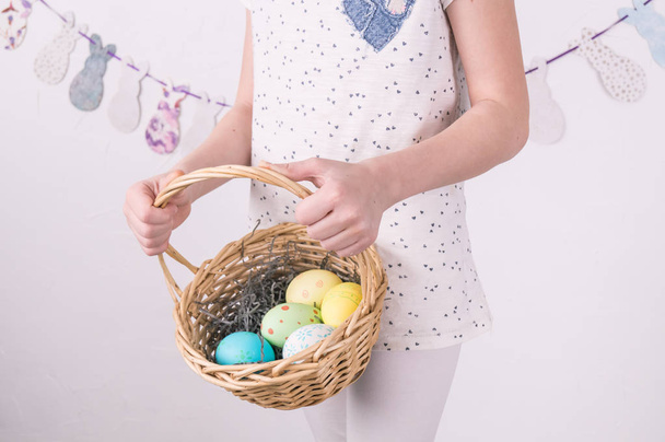 Congratulations on happy Easter: the girl is holding a basket with painted eggs by the white wall. - Fotografie, Obrázek