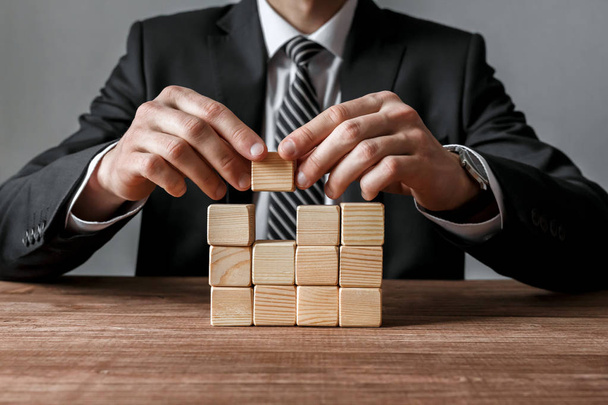 Closeup of businessman making a structure with wooden cubes. Success and business strategy concept. - Fotoğraf, Görsel