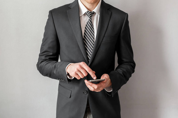 Selbstbewusster Geschäftsmann im Anzug mit Smartphone vor grauem Hintergrund. - Foto, Bild