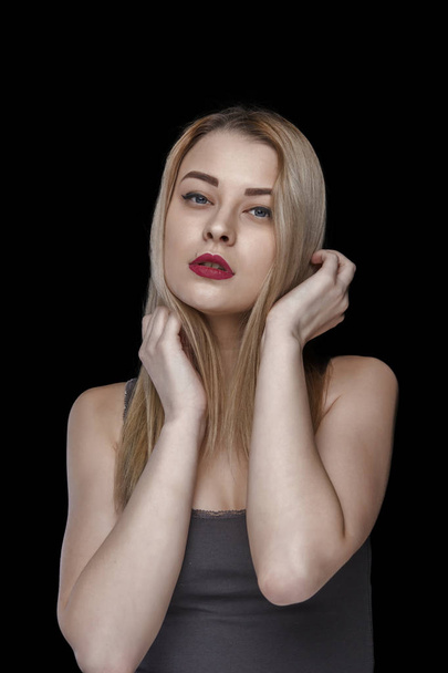 Woman touching head. Red lip makeup, brunette hair, clean skin, blue eyes model girl. Black background - Photo, image