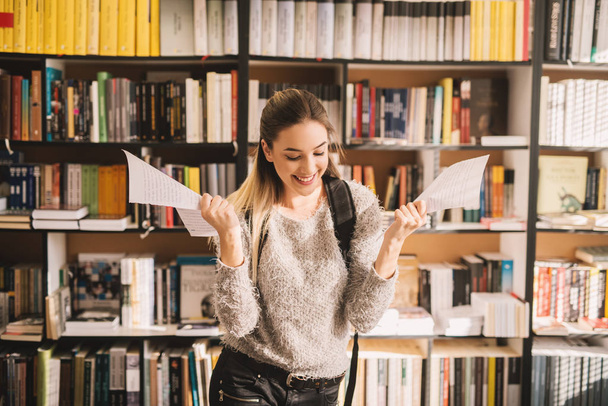 Gelukkig jonge vrouwelijke student houden notities in bibliotheek - Foto, afbeelding