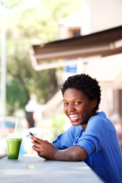 Portrait de belle jeune femme africaine se relaxant au café extérieur avec un téléphone intelligent
  - Photo, image