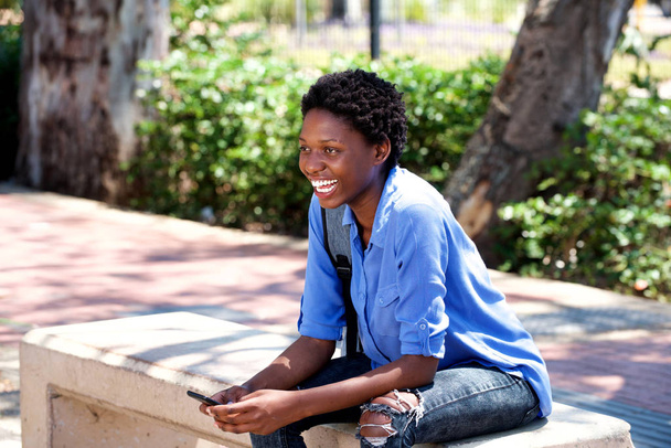 Portrét mladé africké ženy sedí venku s mobilním telefonem a pytel - Fotografie, Obrázek