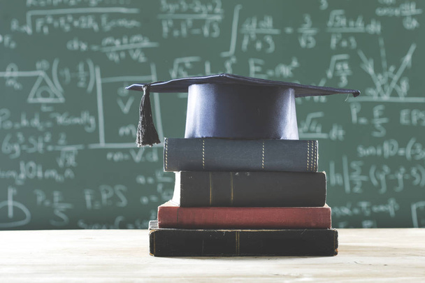 Libros de pila sombrero de graduado en frente de pizarra verde
 - Foto, imagen
