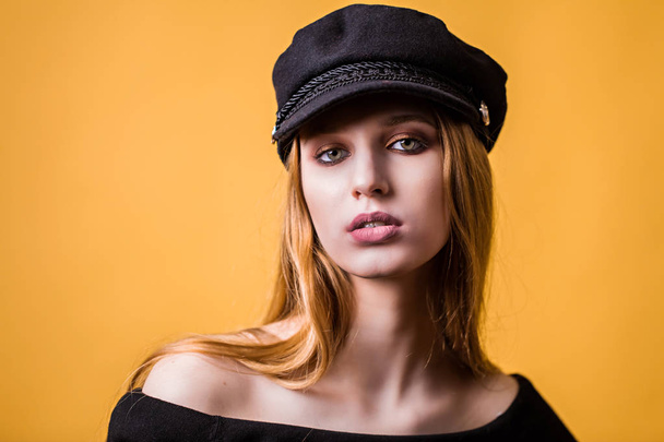 Beautiful woman blonde hair face close up portrait studio on yellow. Girl in black cap looking at the camera - Foto, afbeelding