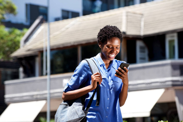 Retrato de sorrir jovem estudante caminhando ao ar livre e ler mensagem de texto no telefone inteligente
 - Foto, Imagem