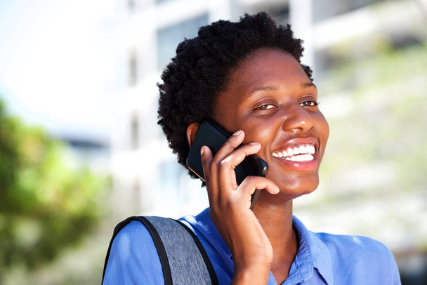 Açık havada akıllı telefonda konuşurken ve gülümseyen güzel genç siyah kadın portresi - Fotoğraf, Görsel