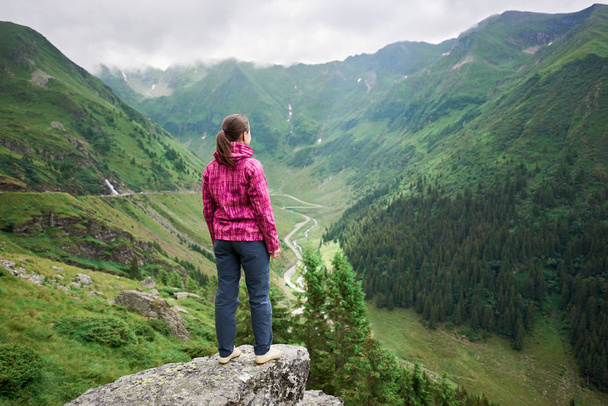 Touriste féminine jouit du beau paysage de la vallée de montagnes verdoyantes, nuages suspendus sur eux et Transfagarashan Highway. La plus belle route d'Europe, Roumanie
 - Photo, image