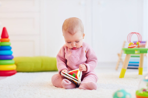 cute little baby girl sitting on the carpet among the development toys, with her first book - Photo, image