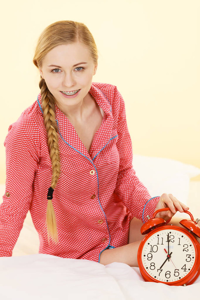 Sleepy woman wearing pajamas holding clock - Foto, Imagem