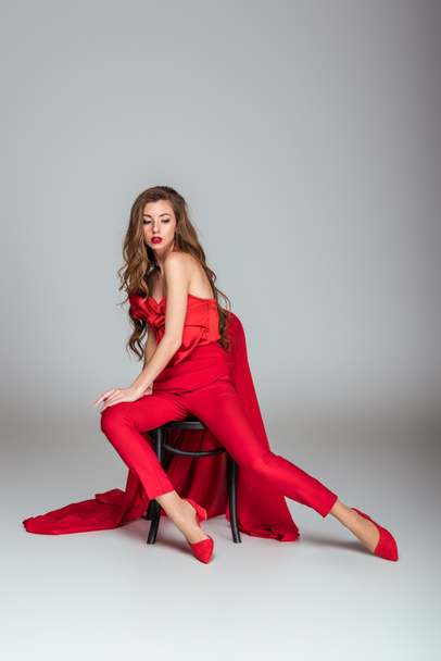 Grey sandalye üzerinde oturan kırmızı giysili güzel moda kadın - Fotoğraf, Görsel