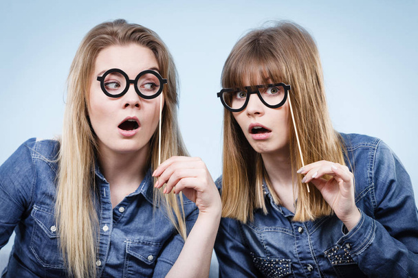 Two happy women holding fake eyeglasses on stick - Fotó, kép