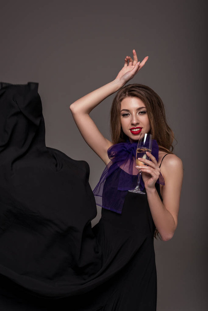 atrakcyjna kobieta stwarzających z lampką szampana dla strzelać moda na szarym tle - Zdjęcie, obraz