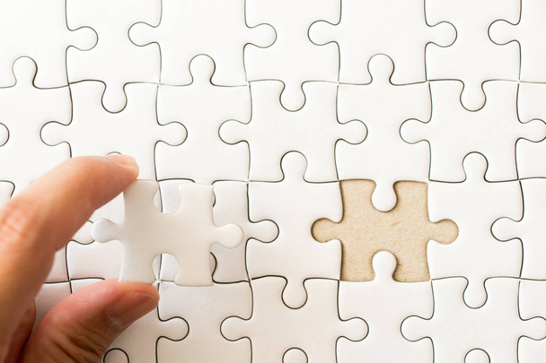 Closed up background of white plain jigsaw with hand that hold missing piece to match or fulfill - Foto, Imagen
