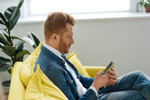 Young man sitting on sofa with smartphone in hands - Фото, зображення