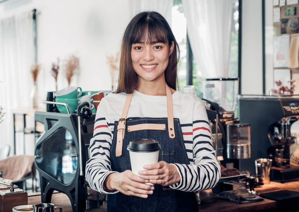asian woman barista wear jean apron holding hot take away coffee - Φωτογραφία, εικόνα