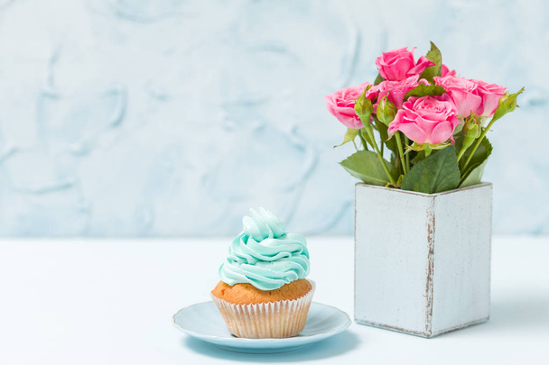 Голубой пастельный горизонтальный баннер с кексом с голубым декором и букет розовых роз в ретро потрёпанной шикарной вазе
. - Фото, изображение
