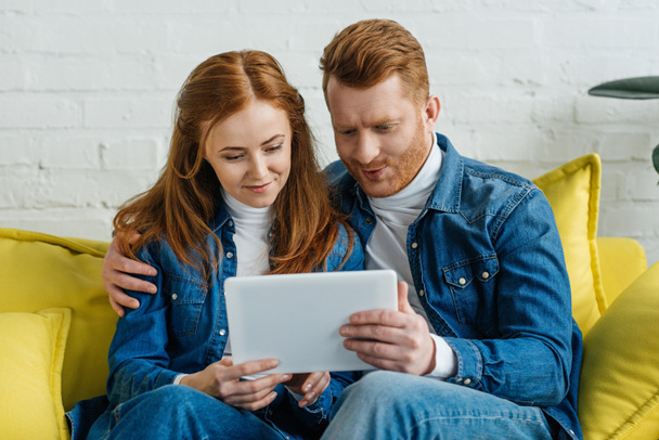 Hombre y mujer mirando la pantalla de la tableta mientras están sentados en el sofá
 - Foto, imagen