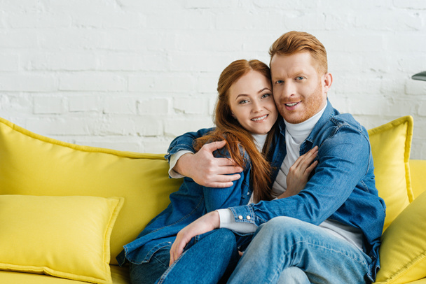 Embracing smiling couple sitting on sofa - Φωτογραφία, εικόνα