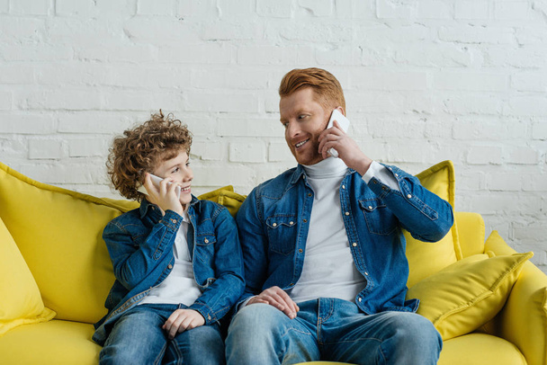 Father and son talking on smartphones while sitting on sofa - Photo, Image