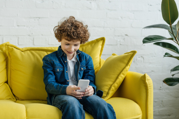 Niño mirando el teléfono mientras está sentado en el sofá
 - Foto, Imagen